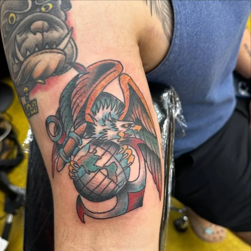 Illustrative color tattoo of an eagle gripping a globe and anchor — the USMC emblem — on the upper arm, by Julian (xwildxlovex) at Ohana Tattoo, Waikiki, Hawaii.