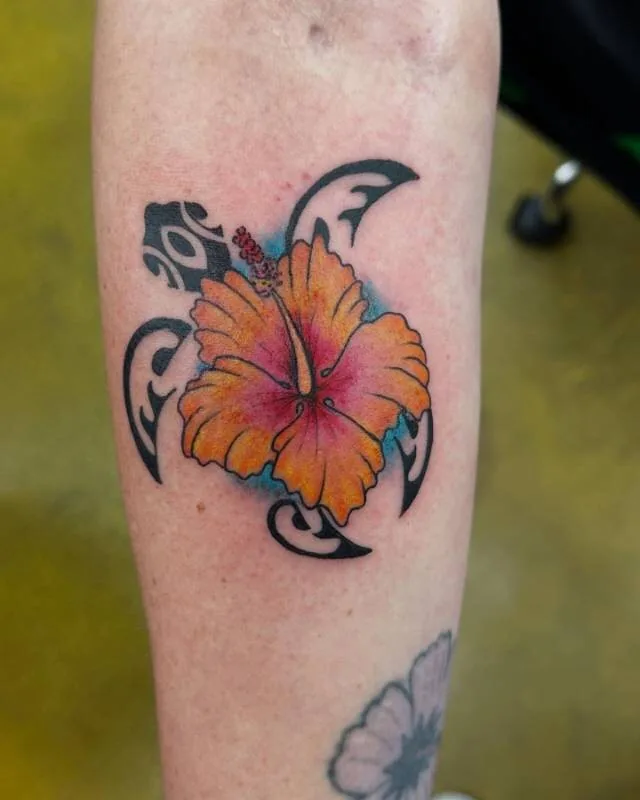 Tattoo of an orange illustrative-color hibiscus inside a black Polynesian honu (sea turtle) silhouette, on the forearm, by Julian (xwildxlovex) at Ohana Tattoo, Waikiki, Hawaii.